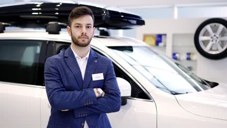 portrait of young car salesman at car showroom, standing with crossed arms