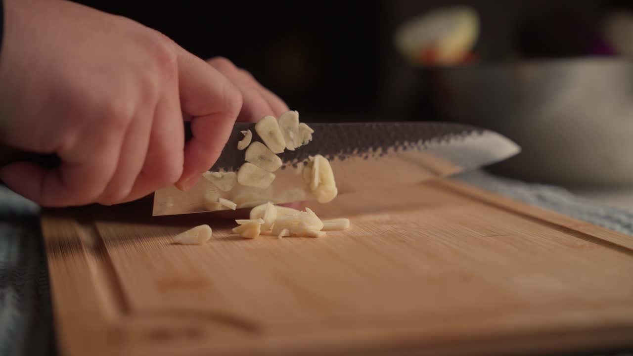 Primo piano di aglio tritato finemente con un coltello da cucina su un tagliere di legno. La scena cattura la preparazione degli ingredienti per un pasto fatto in casa.
