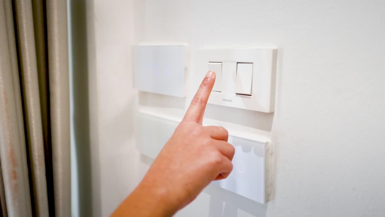 A close-up shot of a finger pressing multiple white plastic light switches on a wall