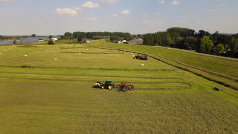 aerial sideways following a tractor with hay tedder producing rows of grass