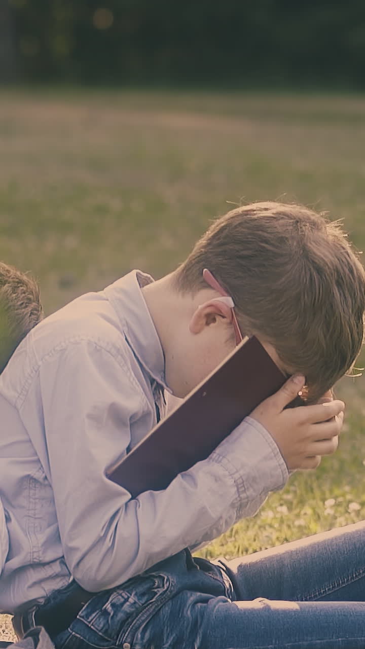 tired junior schoolboy sits with falling textbook on face near sleeping classmate with workbook close view slow motion