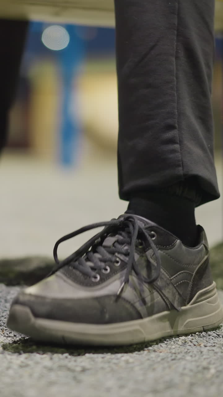 Close-up view of a person's legs, showing them tapping his foot on the ground repeatedly, the background is dimly lit and blurred