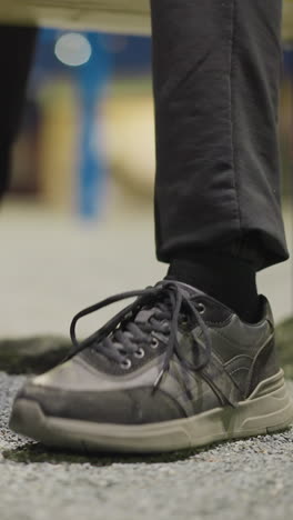 close-up view of a person's legs, showing them tapping his foot on the ground repeatedly, the background is dimly lit and blurred