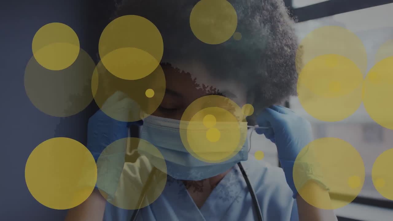 Animation of yellow spots of light over african american female health worker removing face mask