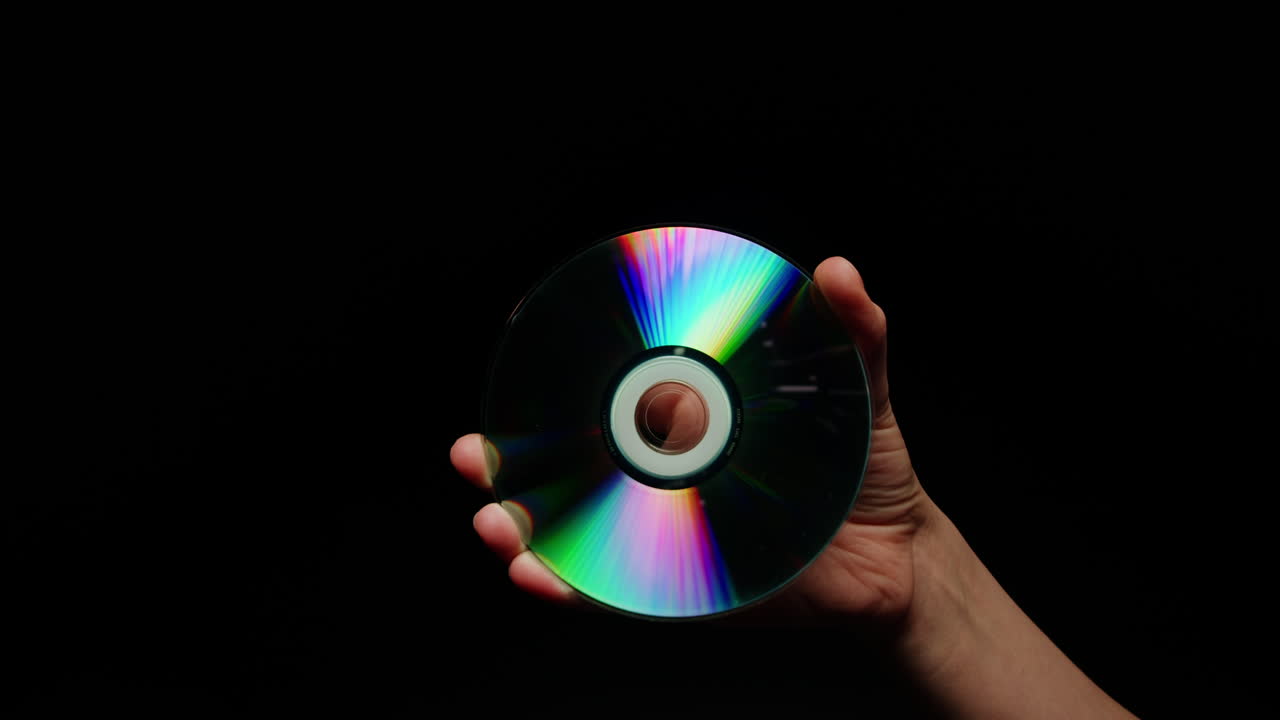 CD disk in hands on black background close-up. Old vintage disks for DVD player or computer. Music recorder, playing retro computer games.