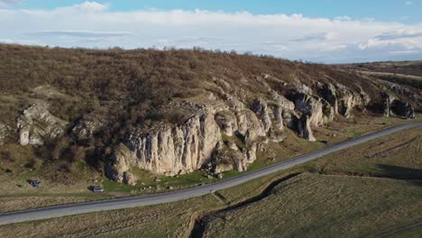 A-scenic-aerial-view-of-a-winding-road-next-to-rocky-cliffs-and-grassy-plains-in-Dobrogea-gorges