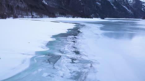 a man walks in a big snowy field in a valley with a lake