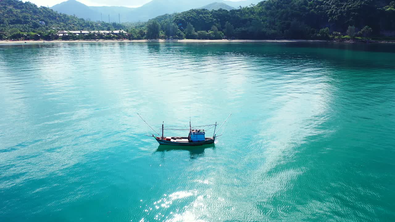 Small fishing boat floating on calm clear water of turquoise lagoon early morning near shore of tropical island with green forest