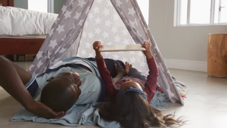 video of happy african american father and daughter lying in tent and using tablet together