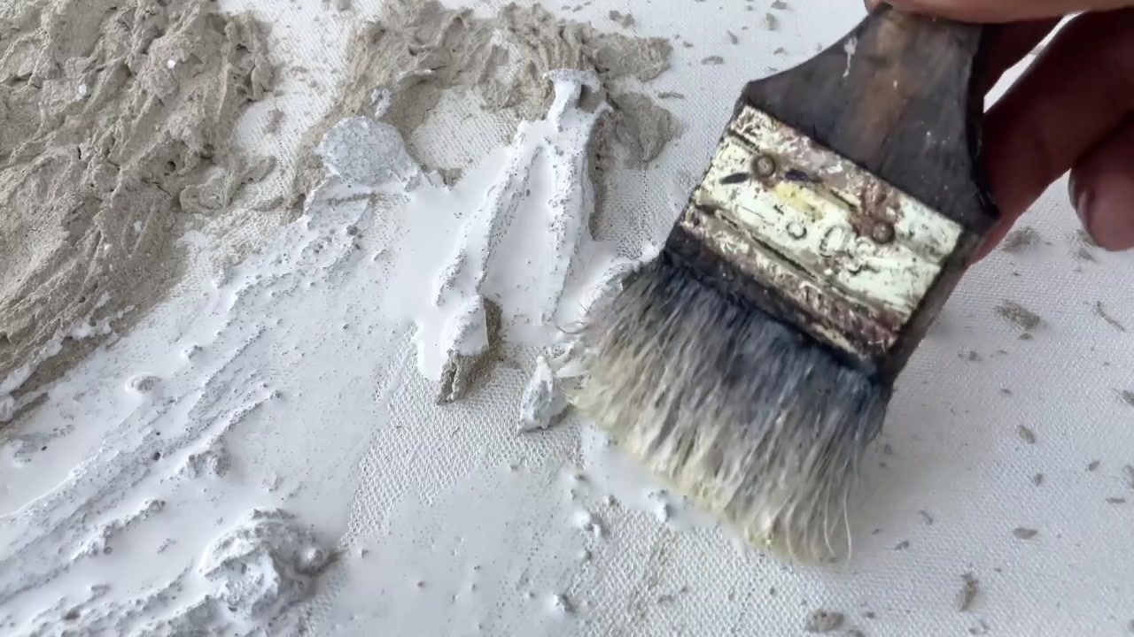 Statische 4K close-up van een kwast die een getextureerd cementen wandkunstwerk wit schildert. Minimalistisch doe-het-zelf woondecoratieproject en creatief proces.