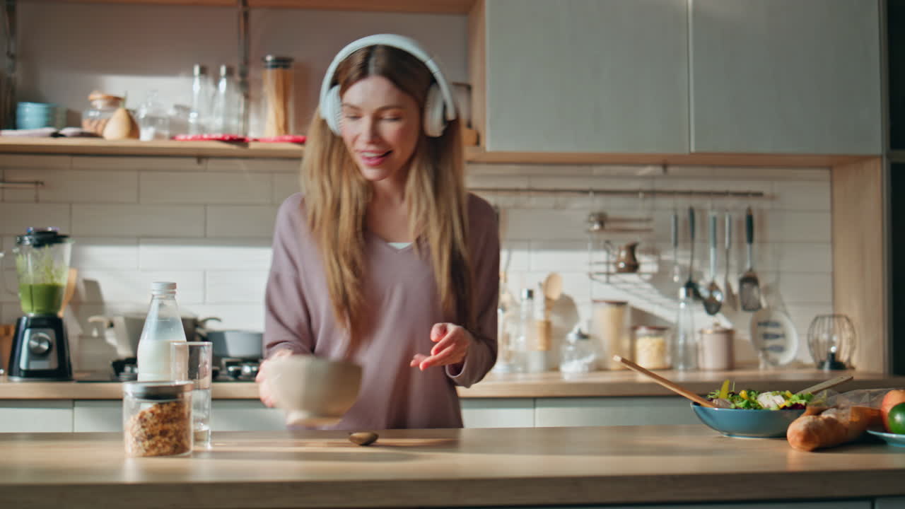 Ragazza con le cuffie che mescola l'insalata ascoltando musica in cucina. Una signora che prepara la colazione.