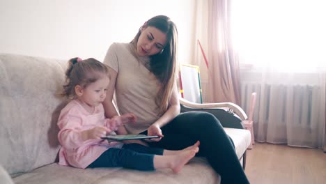 madre e hija están sentadas en el sofá y enseñando usando una computadora tablet