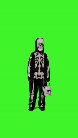 video vertical de larga duración de un niño vestido con un disfraz de esqueleto llamando a la puerta truco o trato en halloween sosteniendo un cubo en forma de calabaza jack o'lantern contra la pantalla verde del estudio 2