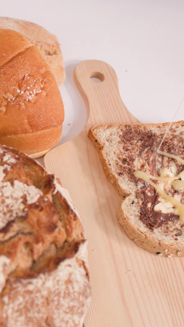 Camera zooms out revealing various breads, croissants, and buttered toast on a wooden board.