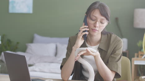 young woman making a phone call and holding her white pet snake while sitting at table at home