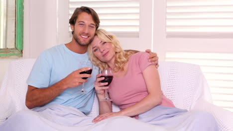 couple sitting on sofa under blanket having red wine