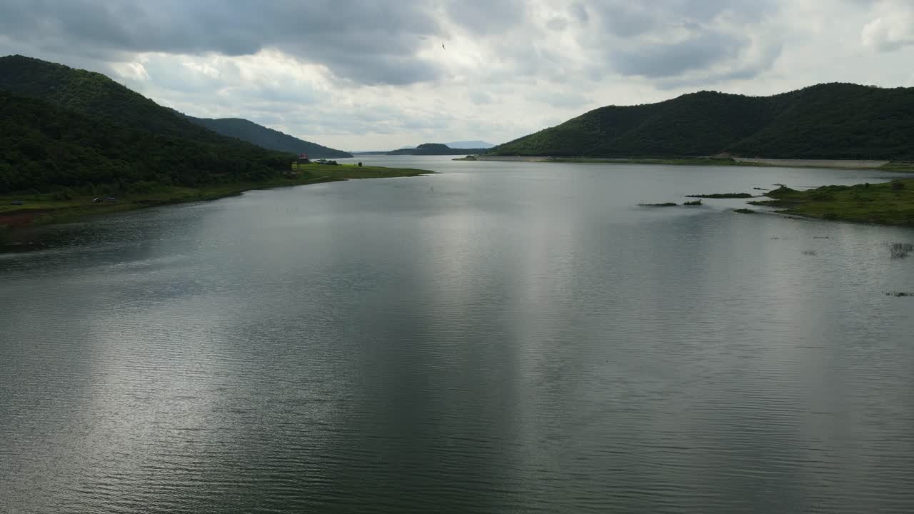 Aerial footage towards the horizon revealing mountains, the dam, a bird passing in front of the camera, the water that reflects the sun setting, Muak Klek, Saraburi, Thailand