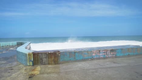 ocean waves crashing against a concrete wall with graffiti