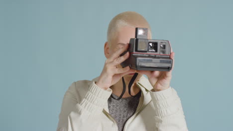 female caucasian model posing with instant film camera against blue backdrop 01