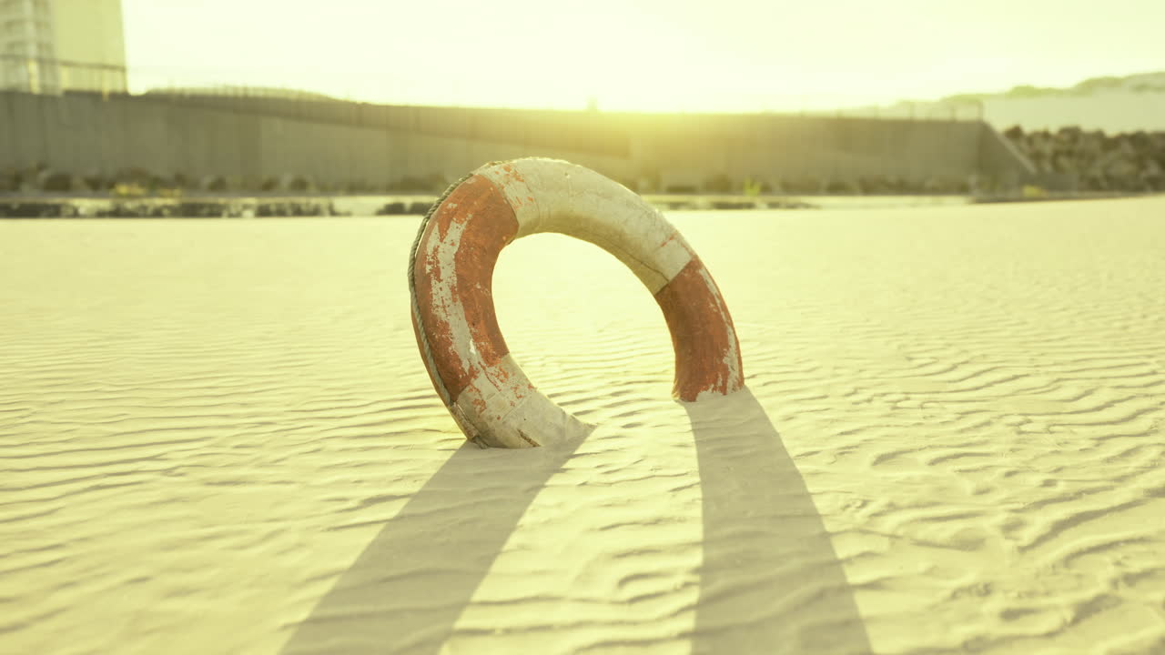 Lifebuoy rests on sunlit beach sand during golden hour near the water