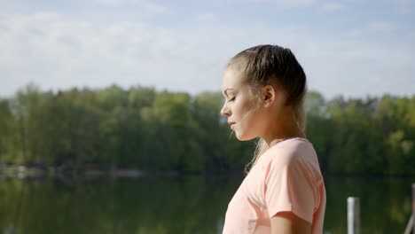Woman-standing-by-lake-breathing-deeply-on-sunny-day
