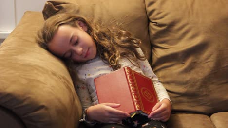 niña pequeña durmiendo en el sofá después de leer un libro