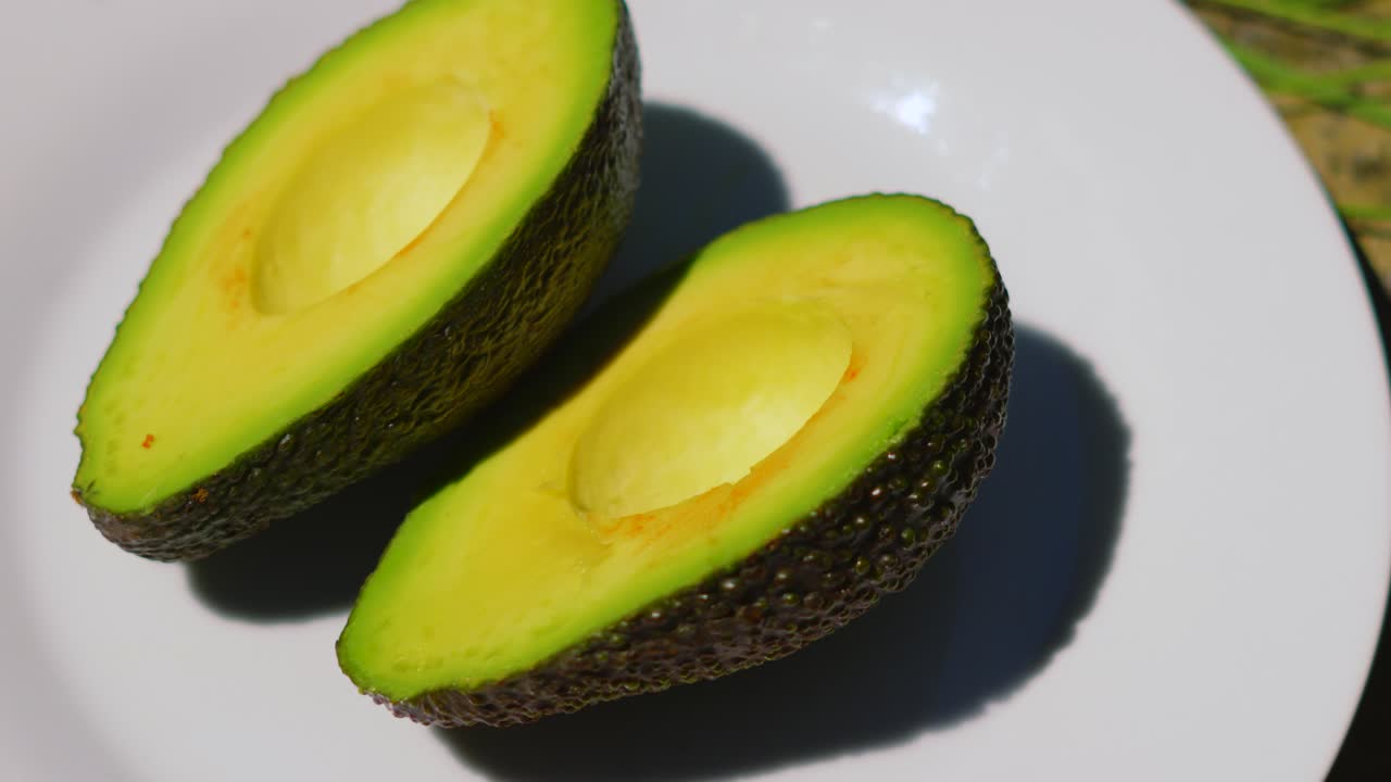 Vista dall'alto di avocado fresco tagliato a metà su piatto bianco sotto la luce naturale del sole all'aperto. Alimento sano, biologico, a base di frutta e verdura. Consumato a colazione o usato nelle salse. Ricco di grassi insaturi benefici per l'intestino.