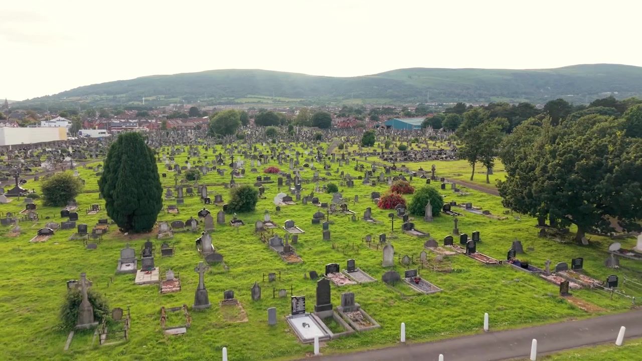 Video aereo 4K a 60FPS in retromarcia lenta del cimitero di Milltown e del lotto repubblicano irlandese sulla Falls Road a Belfast, Irlanda del Nord, Regno Unito. Prodotto con colori Rec709 pronti per la trasmissione