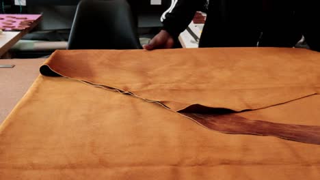 a man folding a large piece of leather on a workbench in a workshop where he created leather goods by hand