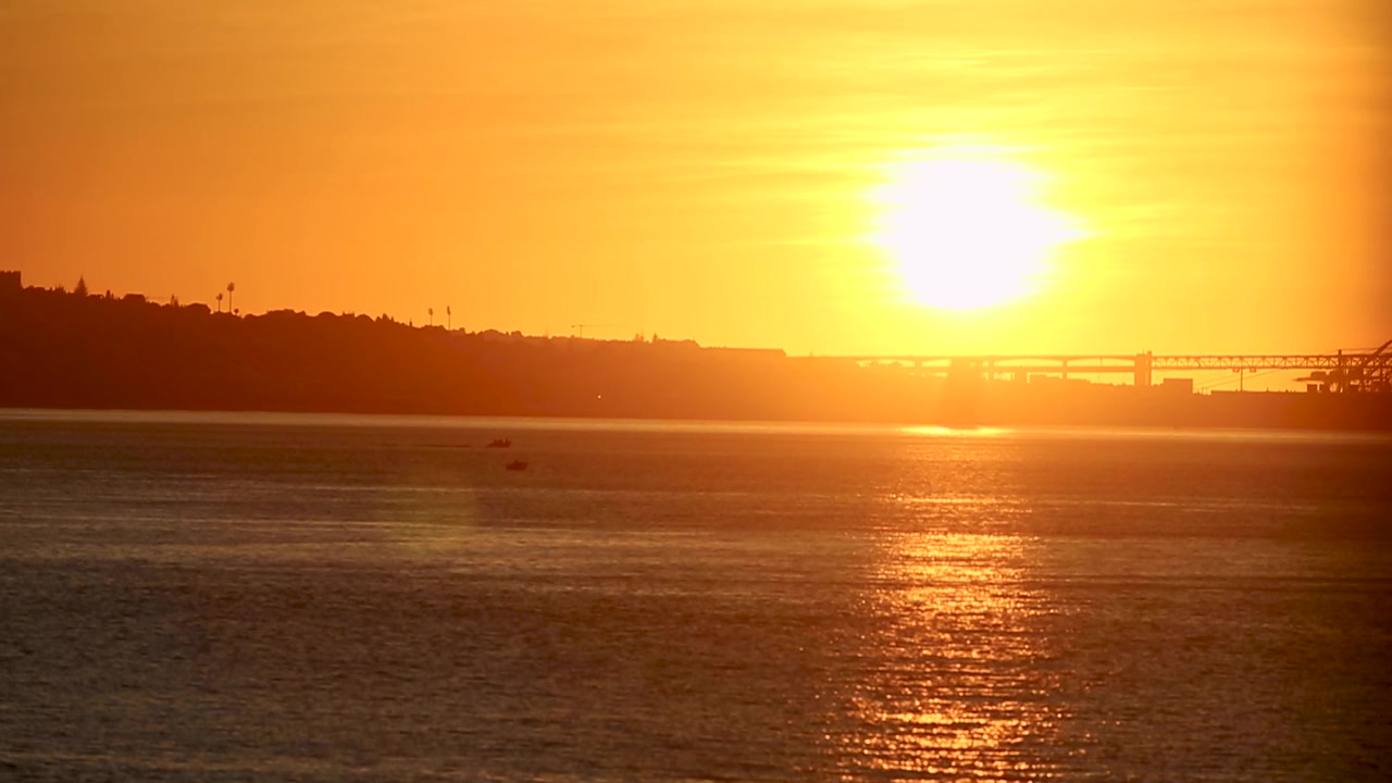 Sunrise over River Tagus in Lisbon with boats floating and 25th April Bridge casting a reflection on the water. Breathtaking view of the city awakening. Portugal.