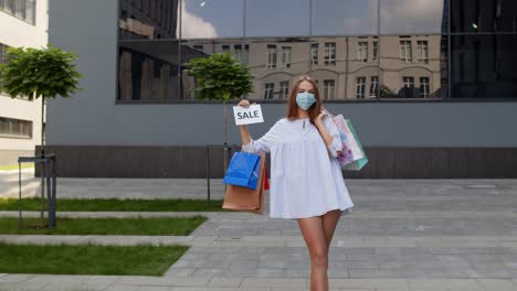 코로나 바이러스 팬데 기간 동안 판매 단어 문구를 보여주는 쇼핑 가방을 가진 보호 마스크를 입은 소녀
