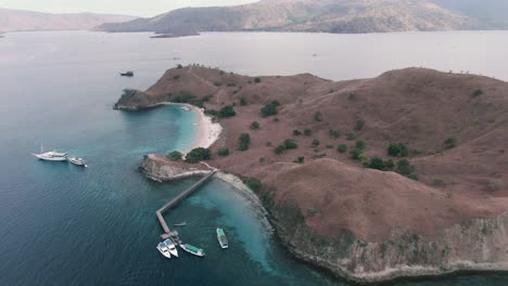 extreme wide clockwise drone shot of tropical komodo island in indonesia with boats, clear blue water, and golden sand beach