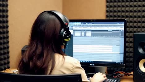 A woman in a professional audio studio, seated at a sleek computer, recording podcast.