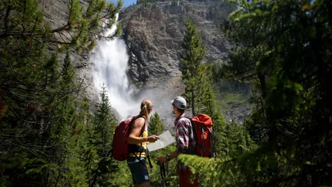 vista frontal de una joven pareja de excursionistas caucásicos con mochila buscando un mapa en el denso bosque 4k