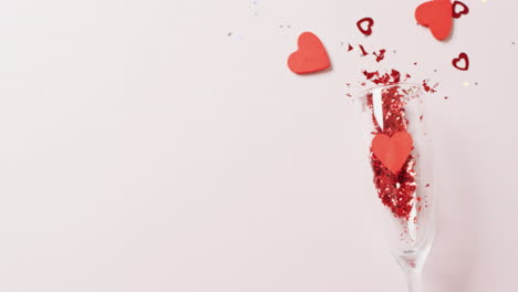 video of champagne glass spilling red heart shapes, on white background with copy space