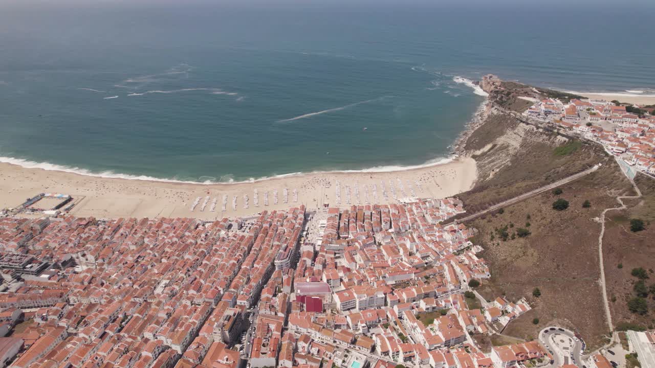 Ripresa aerea in orbita sopra il villaggio di Nazaré e la spiaggia di sabbia bianca in una giornata estiva, Portogallo