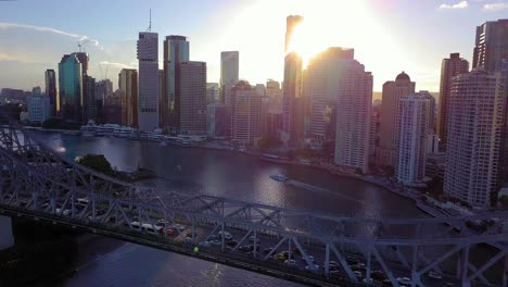 forward aerial view of a city with tall buildings and a car bridge over a river at sunset