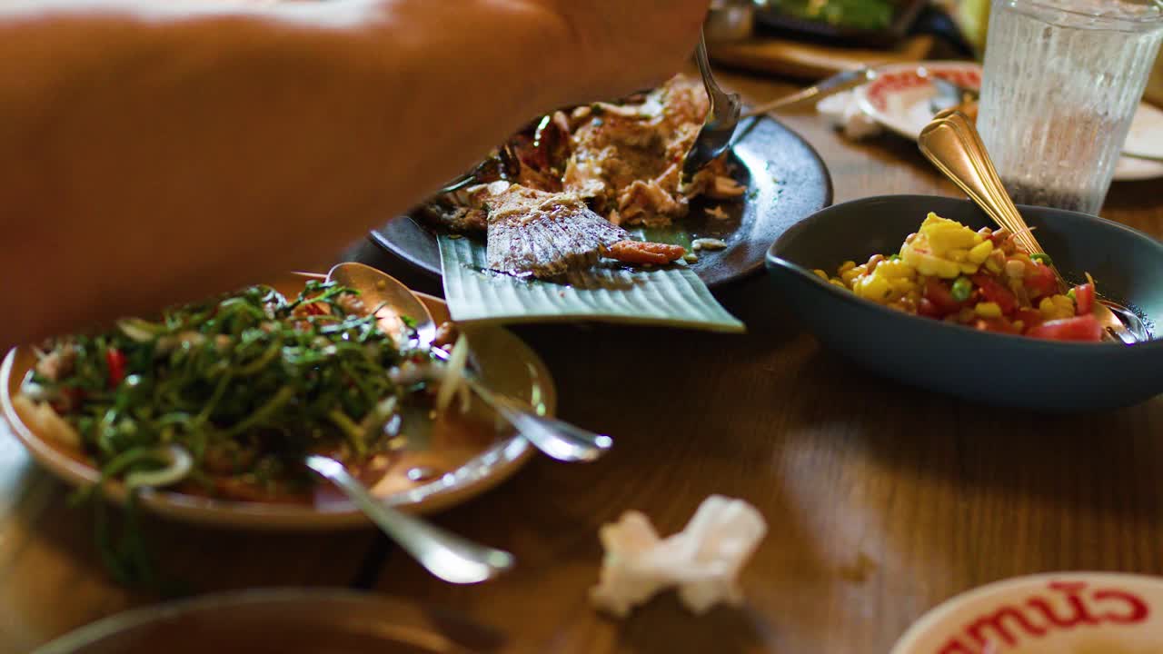 Friends enjoy authentic Thai grilled fish, spicy salad, and rice in a cozy Bangkok restaurant