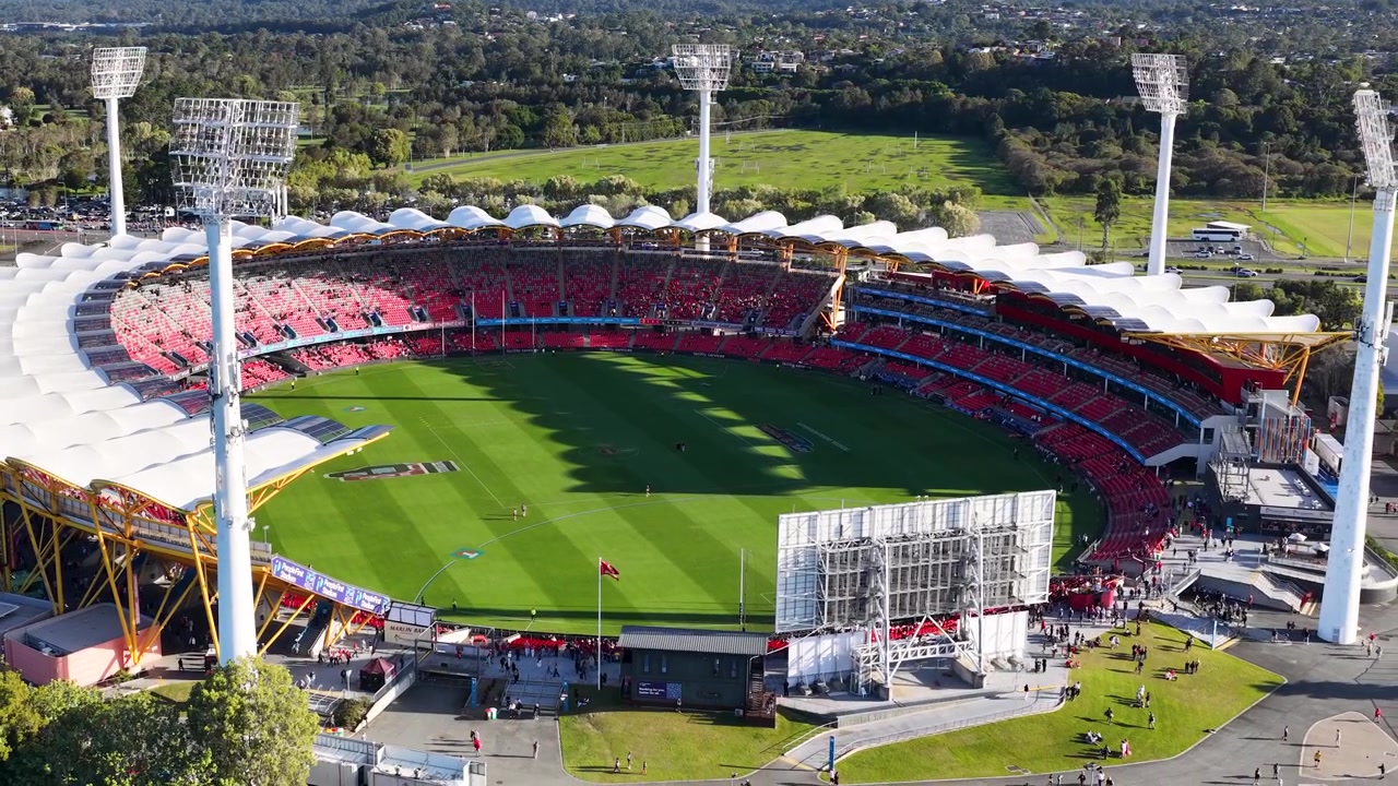 High-angle aerial shot of a circular sports arena with red seating under bright daylight.