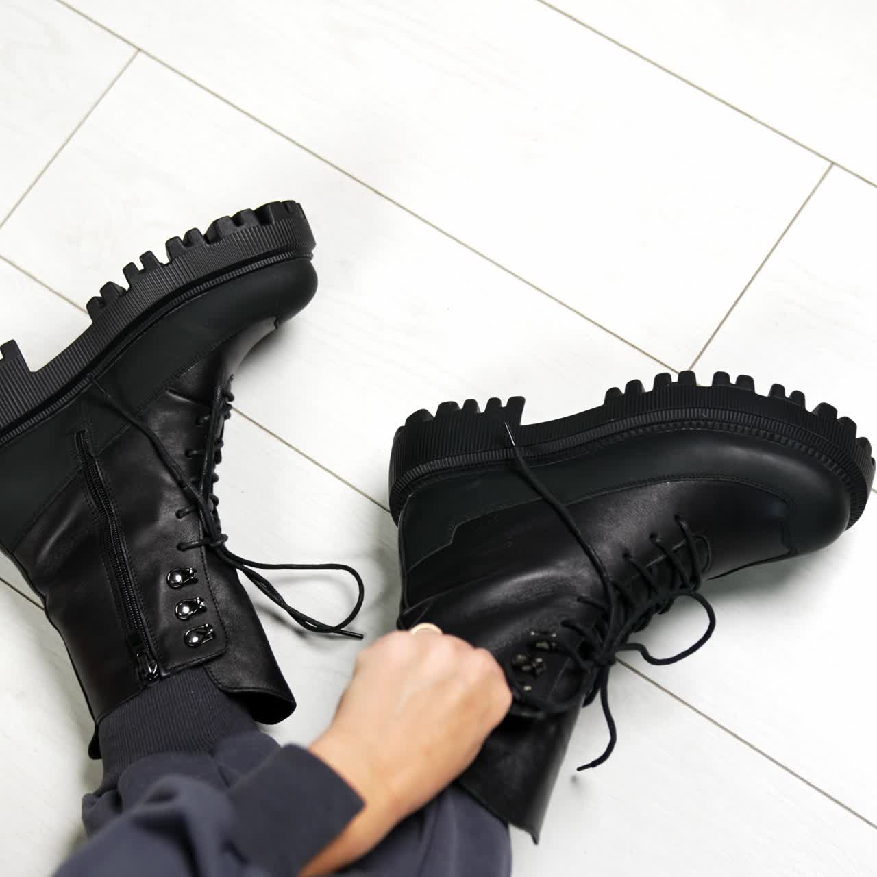 Presentation of black leather stylish army boots with laces. Modern sitting on the floor showing her modern footwear on tractor soles