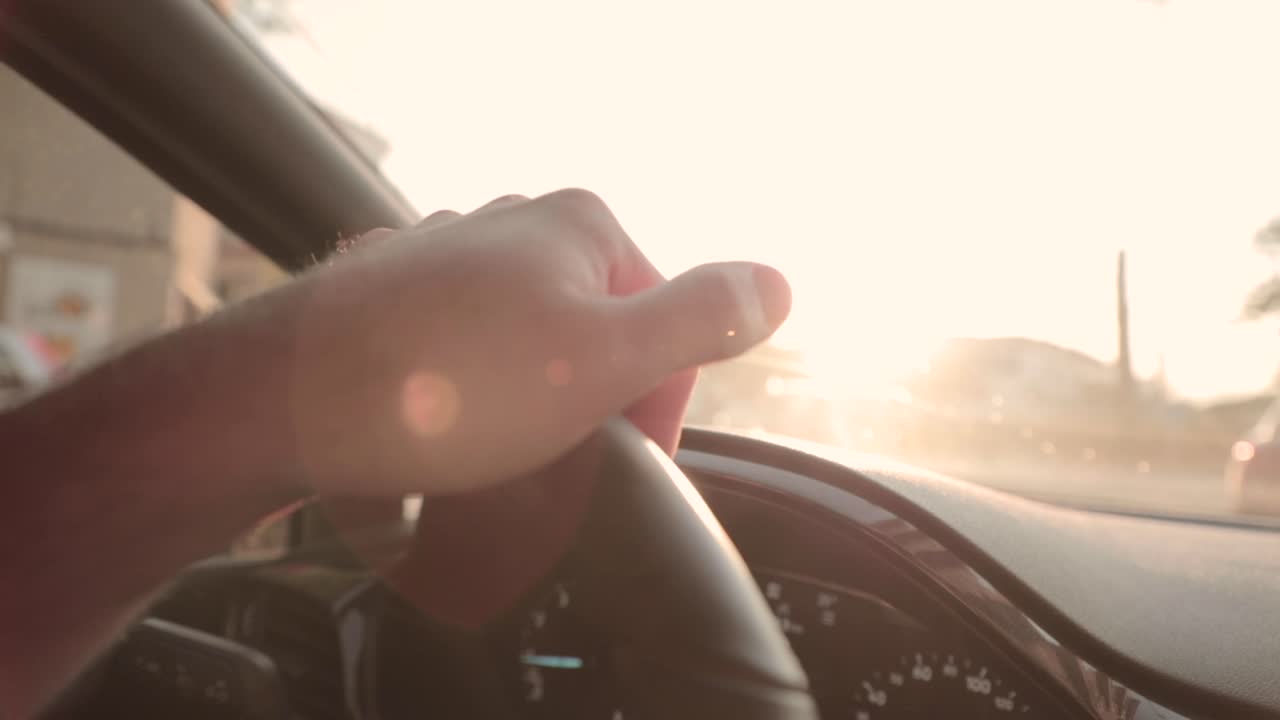 Slow motion, close up on person's hand steering car wheel during golden hour