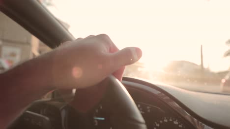 slow motion, close up on person's hand steering car wheel during golden hour