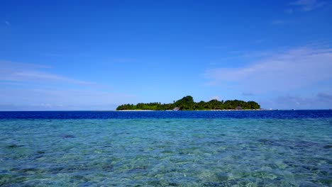 an island in fiji - clear shallow ocean water with lush island in the background - wide shot