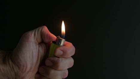 vista cercana de la mano sosteniendo un encendedor e iluminándolo con un fondo negro