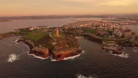 Vista-Aérea-Al-Atardecer-Del-Puerto-De-La-Ciudad-De-La-Coruña-Antiguo-Faro-Romano-Y-Zona-Urbana