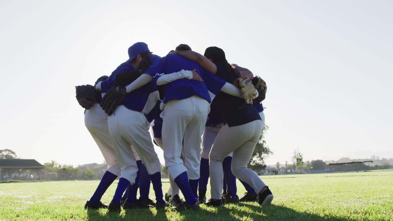 Diverse group of female baseball players in a huddle on sunny pitch