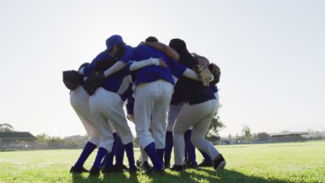 Diverse-group-of-female-baseball-players-in-a-huddle-on-sunny-pitch