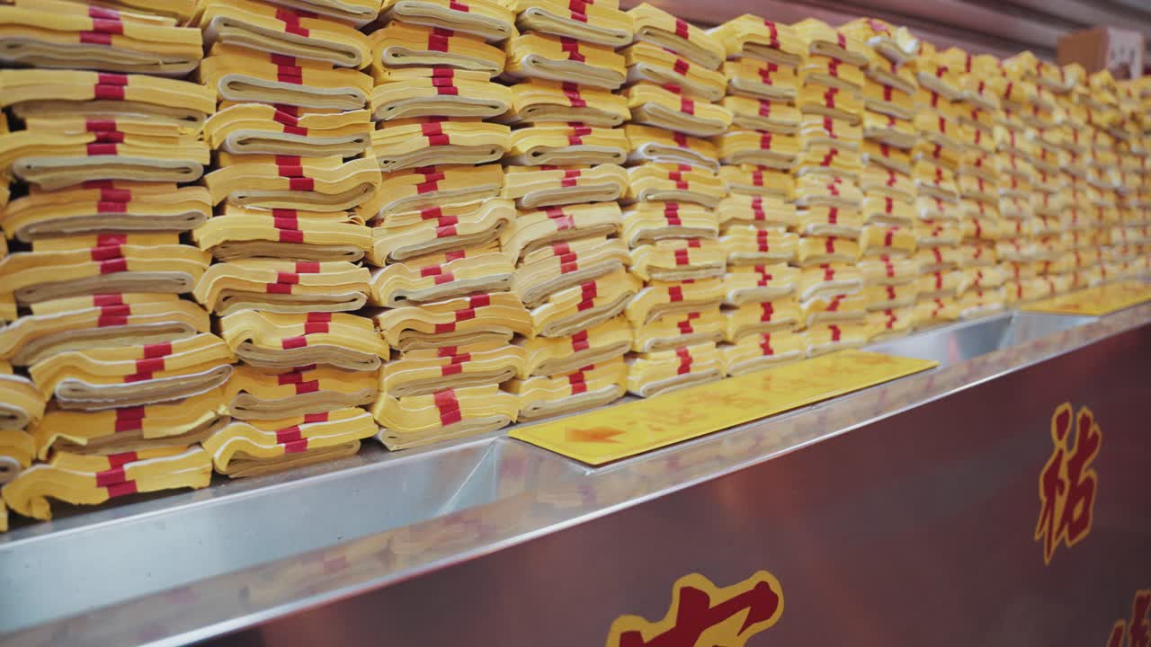 Stacks of folded yellow joss paper with red bindings are neatly arranged at a Taiwanese temple, ready to be burned as spiritual offerings in a traditional ritual honoring ancestors and deities