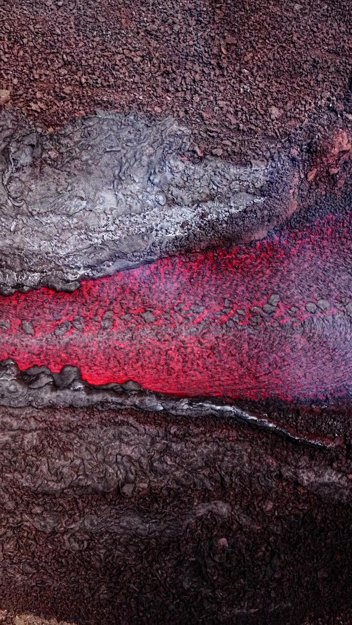 Vista aerea di lava fusa che scorre attraverso un paesaggio vulcanico aspro, con superficie calda visibile.