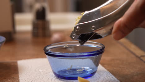 Using-a-press-to-mince-a-clove-of-garlic-into-a-glass-bowl---side-view